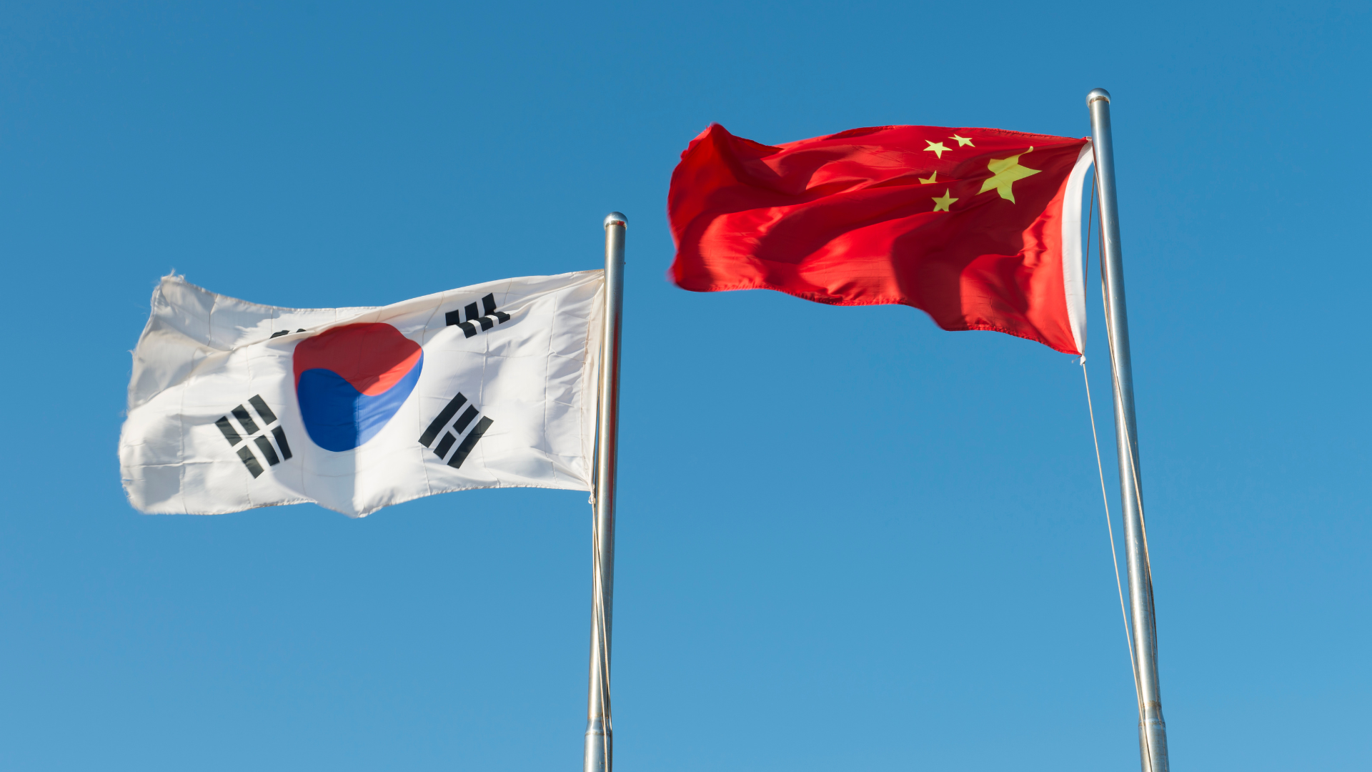 The national flags of South Korea and US flying side-by-side against a clear blue sky.