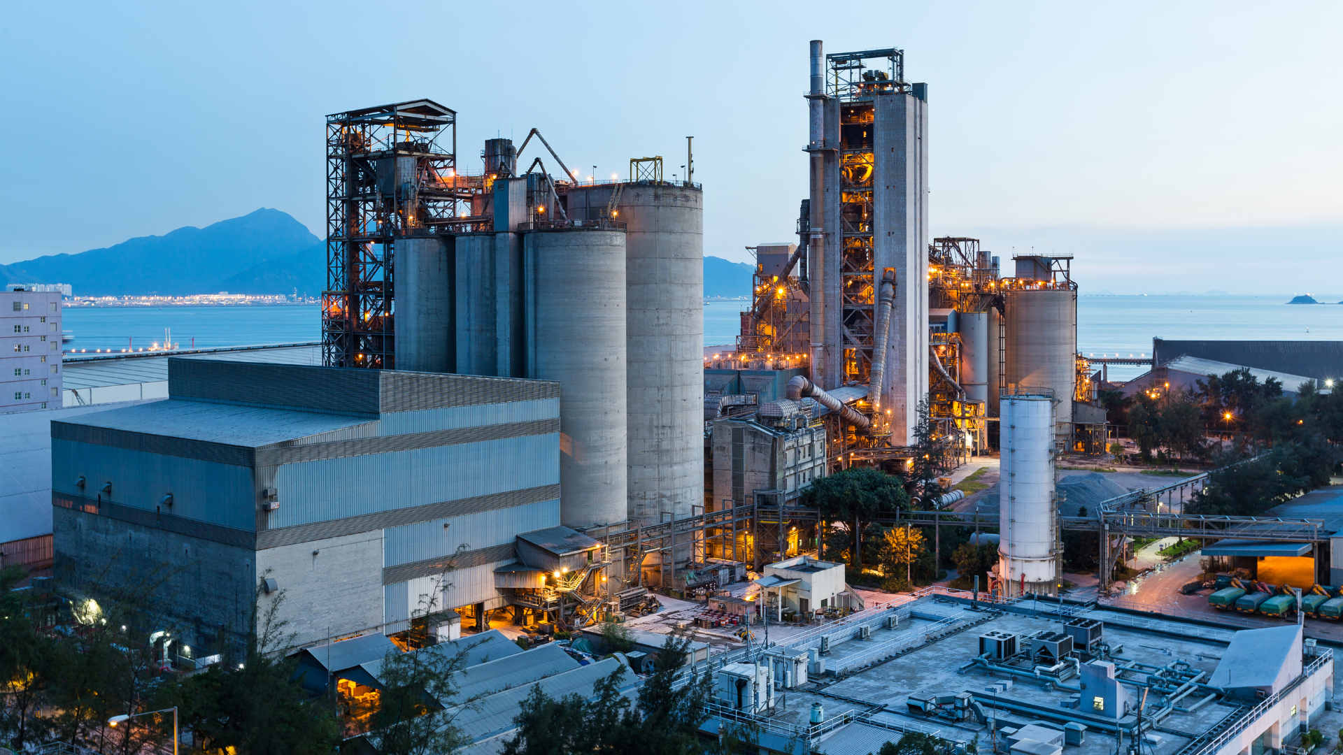 Industrial plant near the coast with large silos and factory structures at dusk.