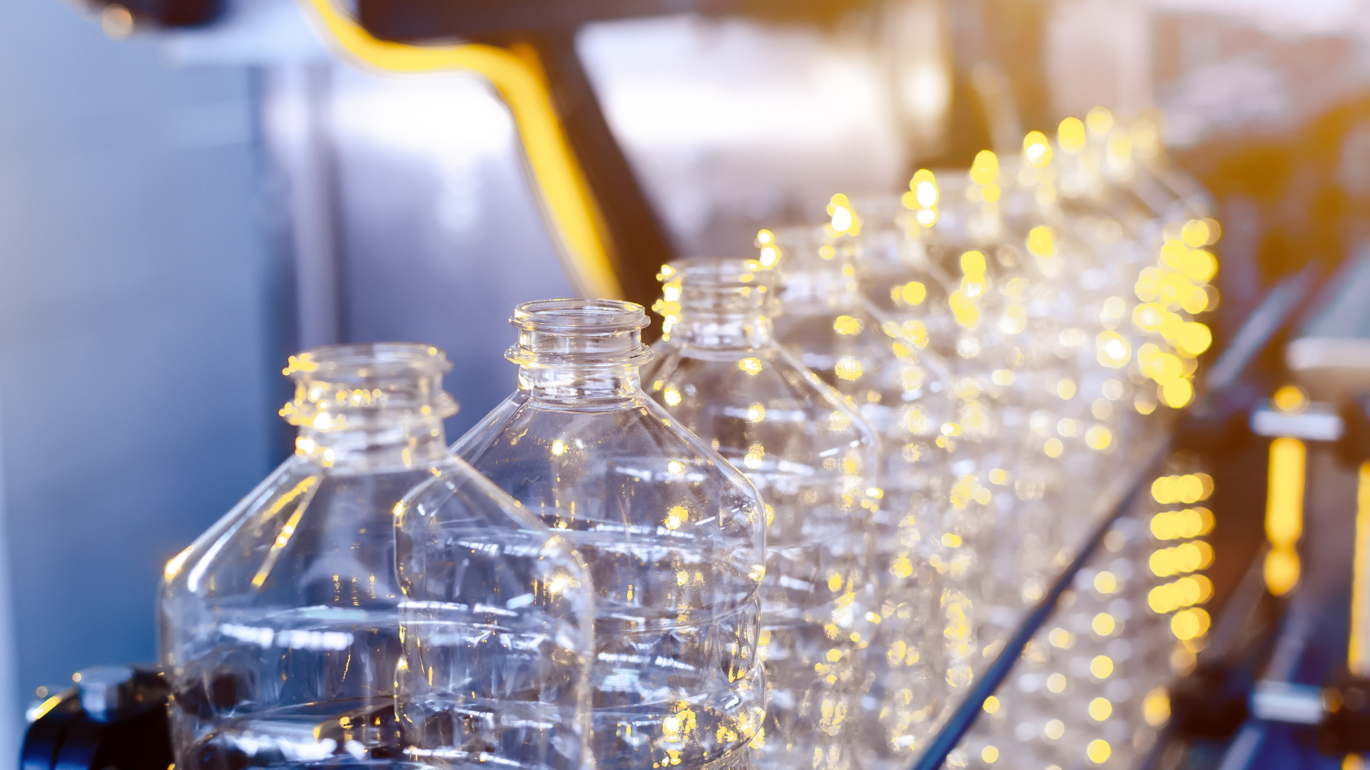 Plastic bottles on an automated production line in a factory, illuminated by warm industrial lighting.