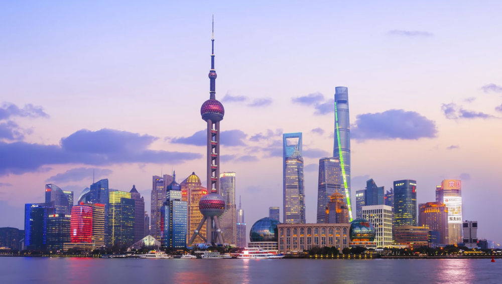 Panoramic view of Shanghai's Pudong skyline at sunset, featuring the Oriental Pearl Tower and Shanghai Tower reflecting in the Huangpu River.