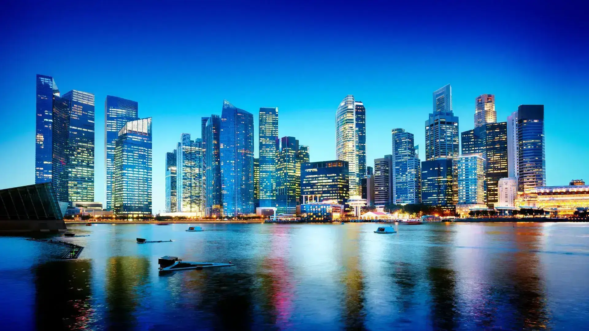 Skyline of Singapore’s central business district at Marina Bay with illuminated skyscrapers reflecting on the water.